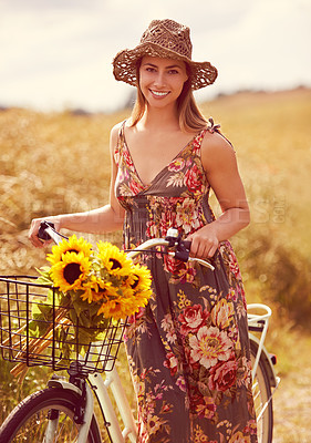 Buy stock photo Shot of a young woman cycling through the countryside with a bunch of sunflowers