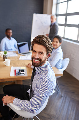 Buy stock photo Portrait of a young businessman sitting around a table with his colleagues in the boardroom