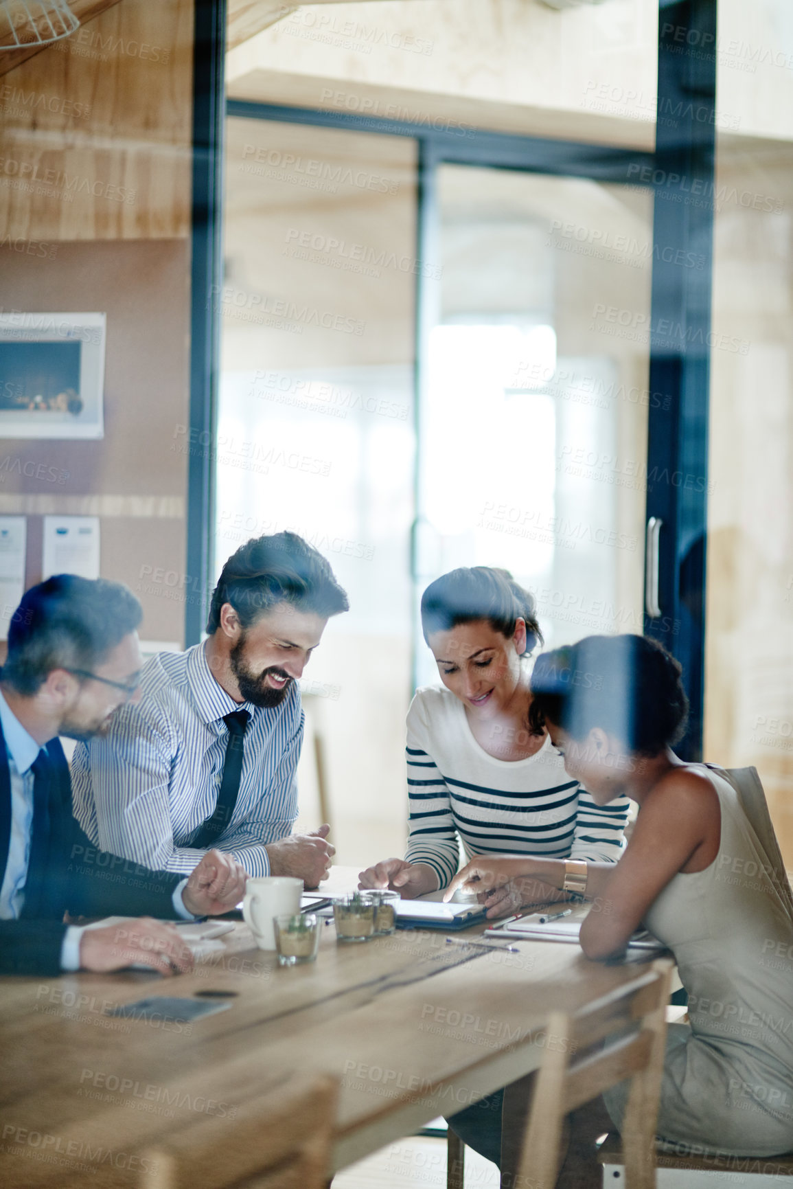 Buy stock photo Through the glass shot of a group of colleagues working together in an office