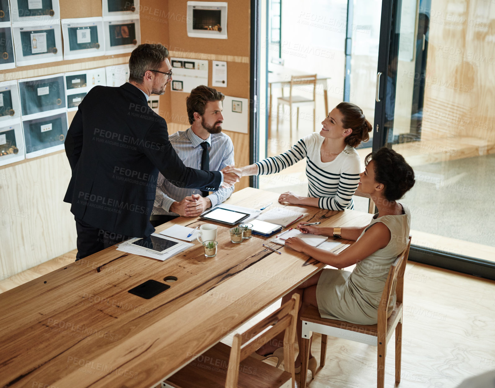 Buy stock photo Shot of two businesspeople shaking hands in an office while colleagues look on