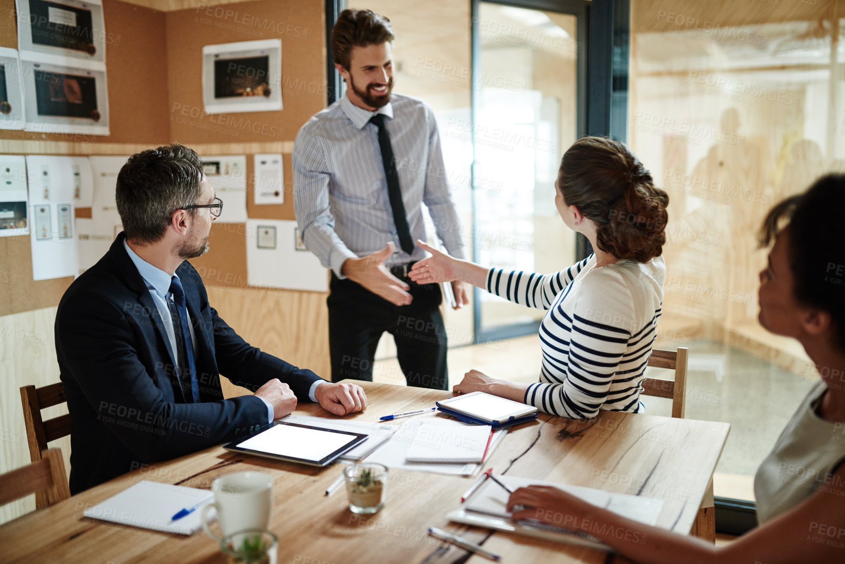 Buy stock photo Shot of two businesspeople shaking hands in an office while colleagues look on