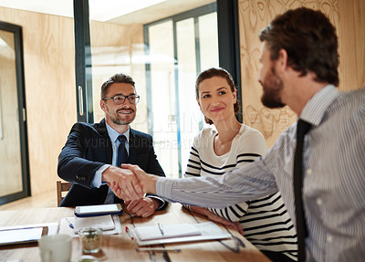 Buy stock photo Shot of two businesspeople shaking hands in an office while a colleague look on