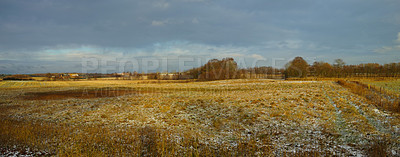 Buy stock photo Landscape of a field on a winter day with a bit of snow on the grass and a cloudy sky. Dry tan grass in an open meadow. Rural countryside with brown pasture melting snow and trees on horizon