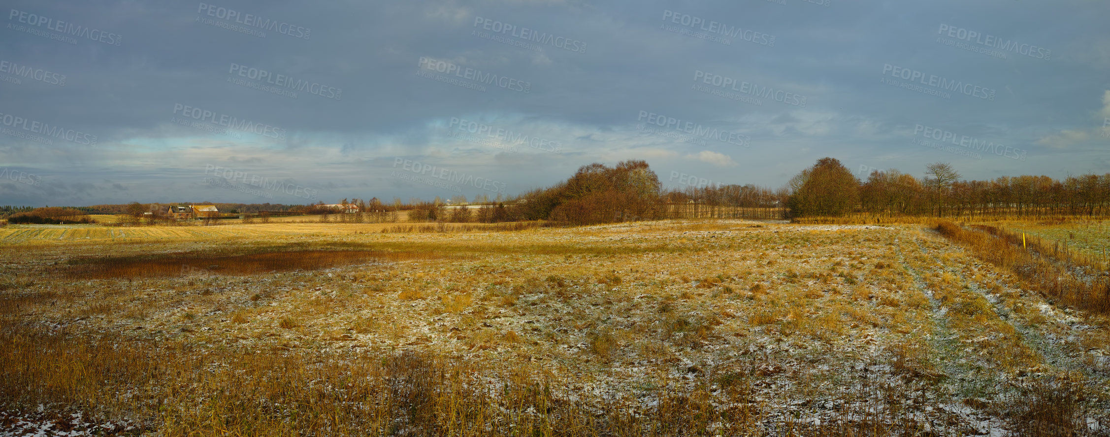 Buy stock photo Landscape of a field on a winter day with a bit of snow on the grass and a cloudy sky. Dry tan grass in an open meadow. Rural countryside with brown pasture melting snow and trees on horizon