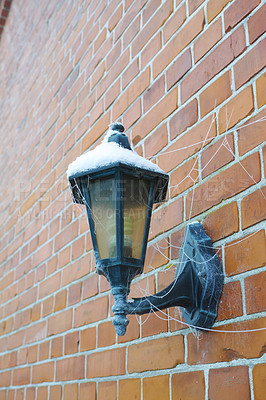 Buy stock photo Closeup of a spider web wrapped around a snow covered street lamp on a red brick wall in a city during winter. Cobweb on an old abandoned electric lantern downtown during snowfall winter weather.