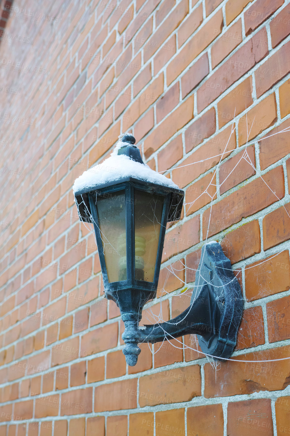 Buy stock photo Closeup of a spider web wrapped around a snow covered street lamp on a red brick wall in a city during winter. Cobweb on an old abandoned electric lantern downtown during snowfall winter weather.