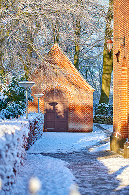 Buy stock photo Exterior of an old church building with snow covered trees and pathway. Small chapel in snowy landscape with sun shining on brick wall. Countryside with European style architecture in winter scene