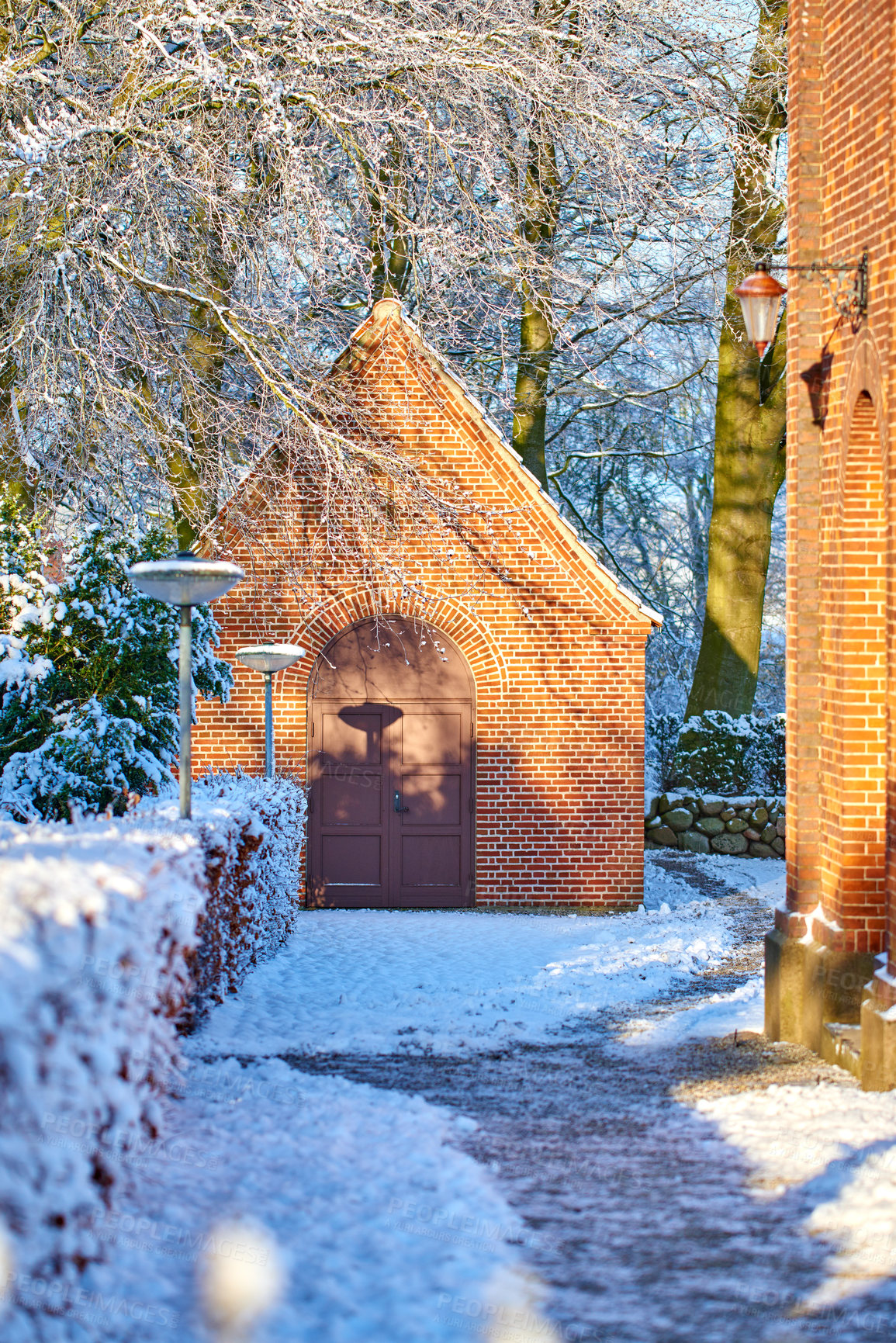 Buy stock photo Exterior of an old church building with snow covered trees and pathway. Small chapel in snowy landscape with sun shining on brick wall. Countryside with European style architecture in winter scene