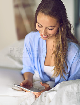 Buy stock photo Shot of a young woman relaxing with her tablet in the bedroom