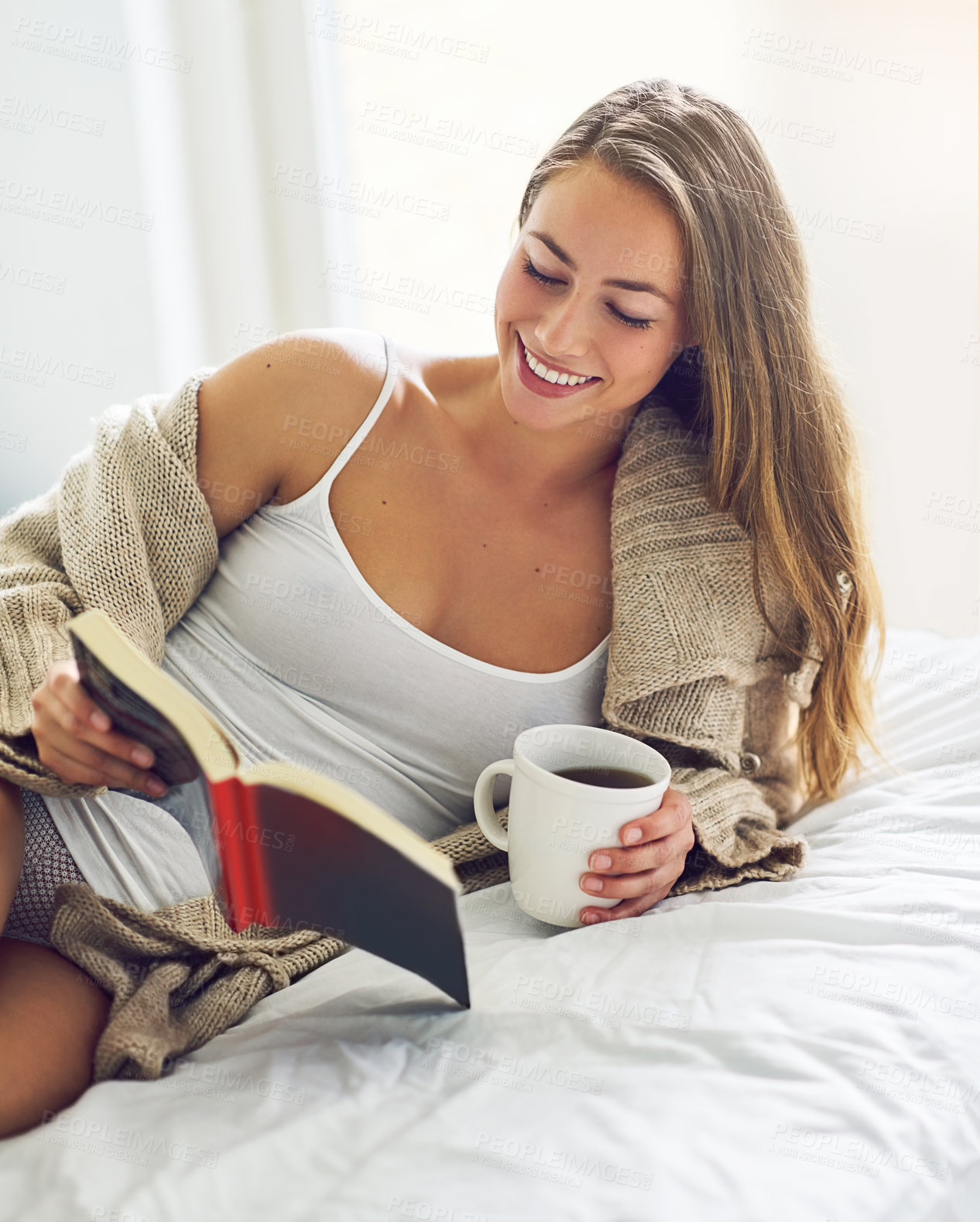 Buy stock photo Shot of a young woman drinking coffee and reading a book in the morning