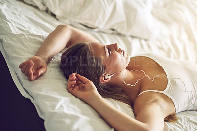 Buy stock photo Shot of a young woman listening to music while relaxing on her bed