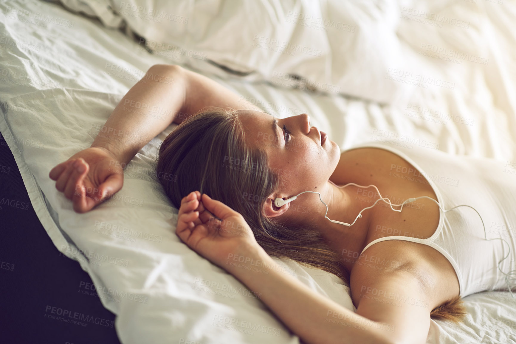 Buy stock photo Shot of a young woman listening to music while relaxing on her bed