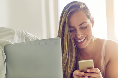 Buy stock photo Shot of a young woman using a laptop and phone in the morning at home