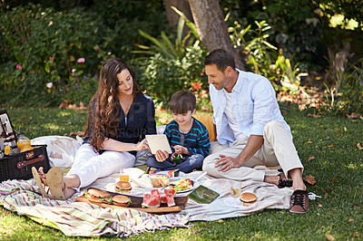 Buy stock photo Parents, boy and picnic at park with tablet, smile and relax on lawn with movies, games and bonding in summer. Mother, father and son with touchscreen, food and video on blanket with family in Italy