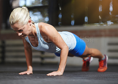 Buy stock photo Shot of a young woman doing pushups in a gym