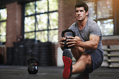 Buy stock photo Shot of a young man working out with a kettlebell in a gym