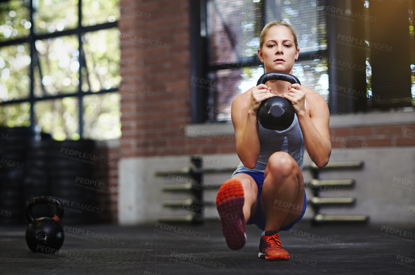 Buy stock photo Shot of a young woman working out with a kettlebell in a gym