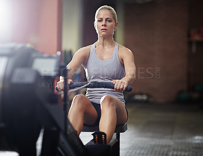 Buy stock photo Shot of a young woman working out on a rowing machine in a gym