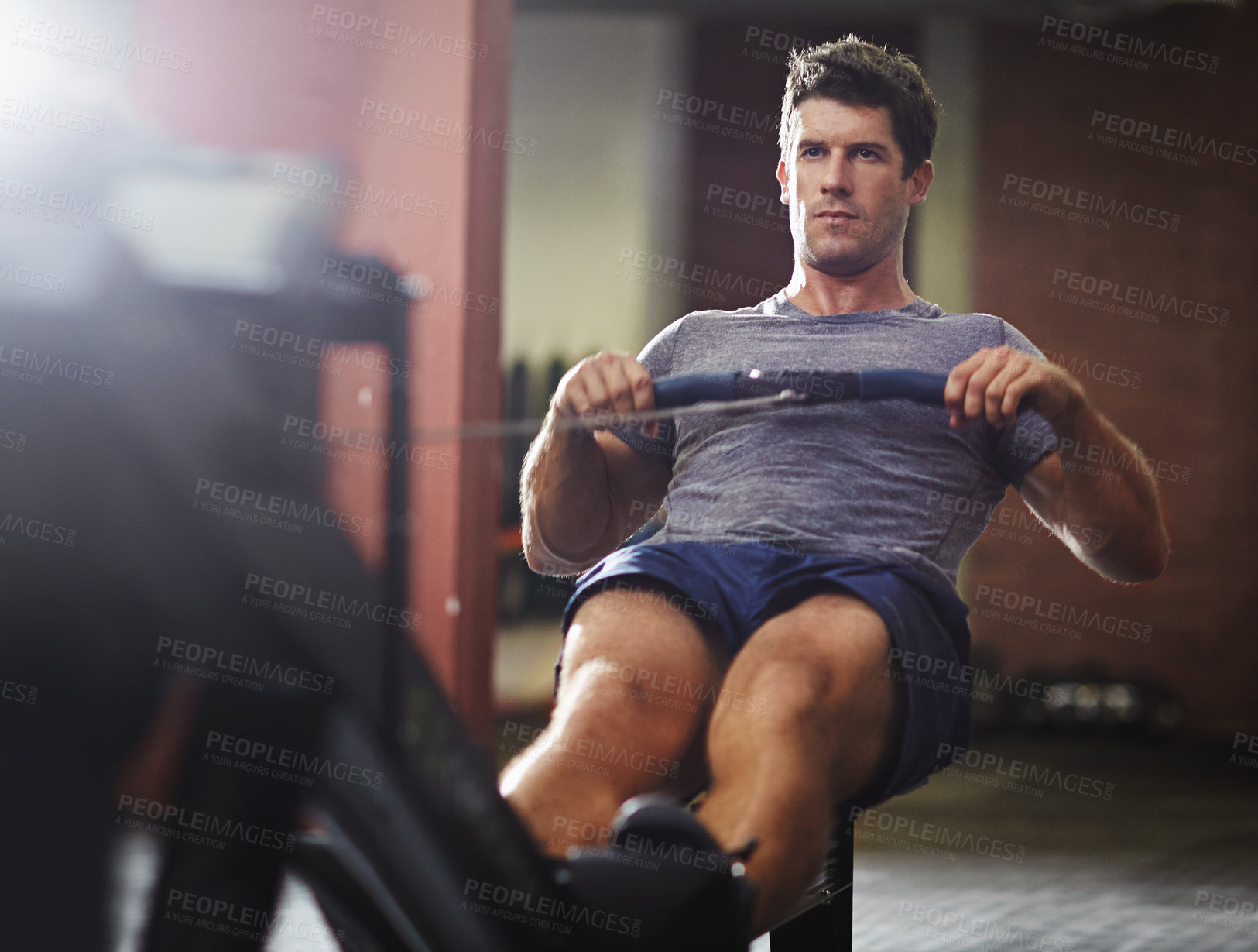 Buy stock photo Shot of a young man working out on a rowing machine in a gym