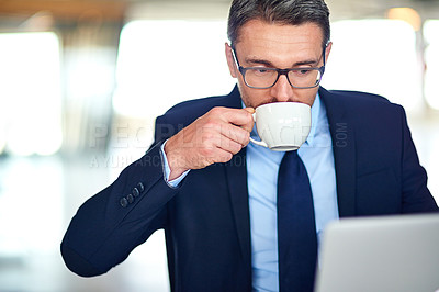 Buy stock photo Shot of a businessman drinking coffee and using a laptop in the office