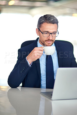 Buy stock photo Shot of a businessman drinking coffee and using a laptop in the office