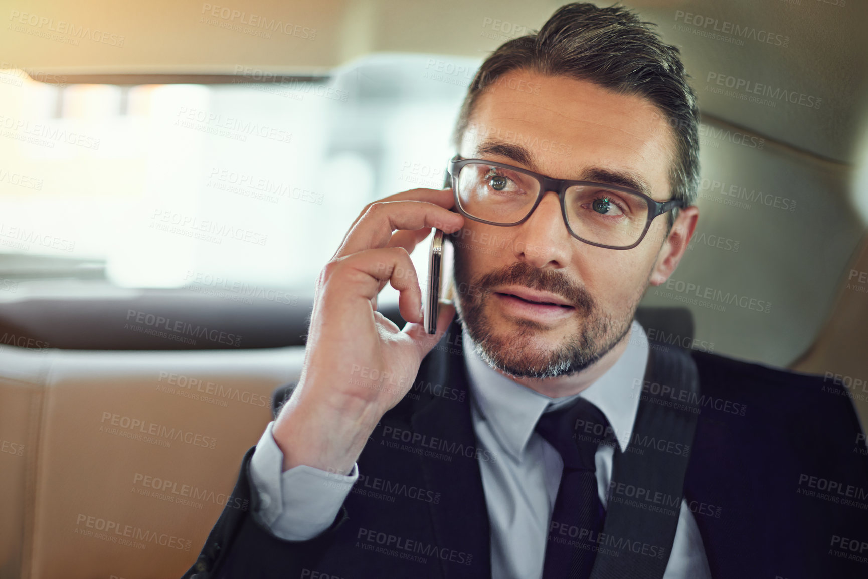 Buy stock photo Cropped shot of a businessman using his cellphone while sitting in the backseat of a car