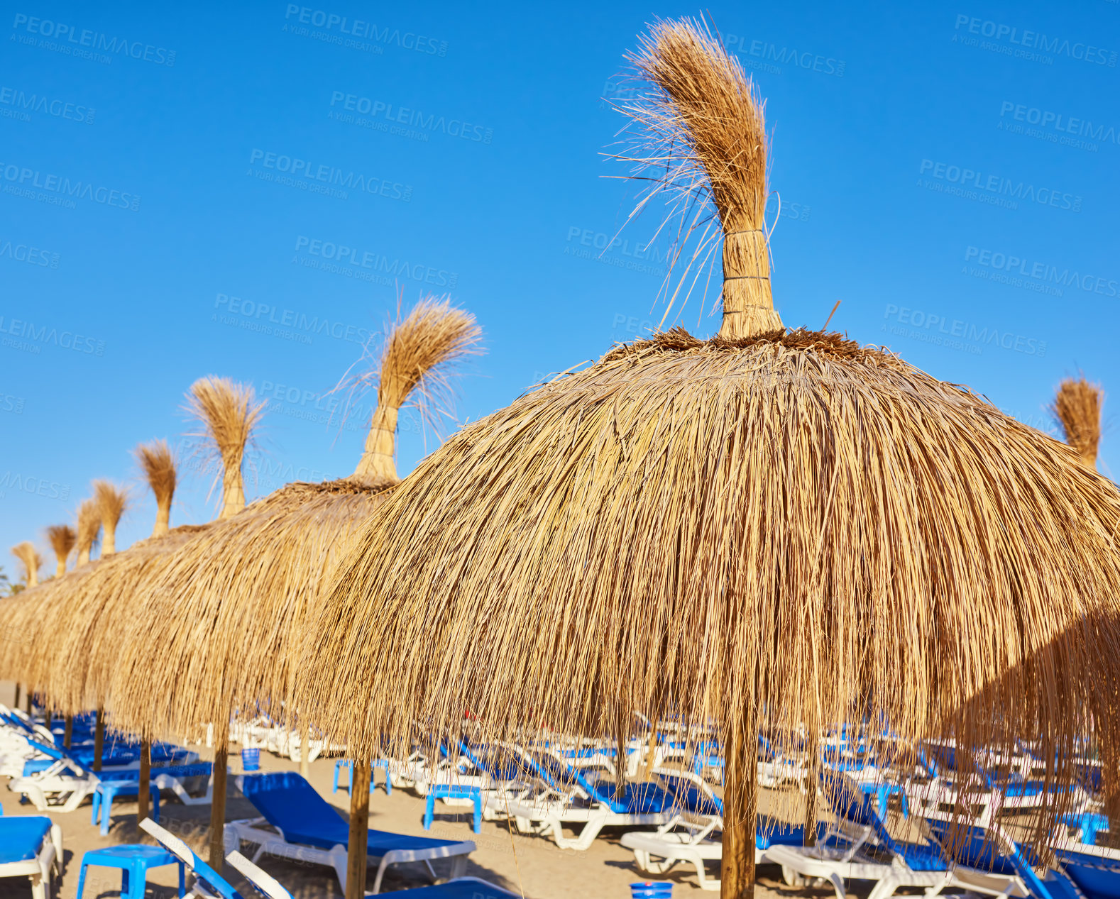 Buy stock photo Straw umbrella, chairs and blue sky at beach for travel, shade or service at luxury resort. Thatch sunshade, seats or sunshine at ocean for holiday, vacation or eco friendly design for relax in Spain