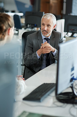 Buy stock photo Shot of two coworkers sitting at their workstations talking together