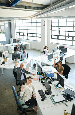 Buy stock photo Portrait of a group of waving coworkers sitting at their workstations in an office