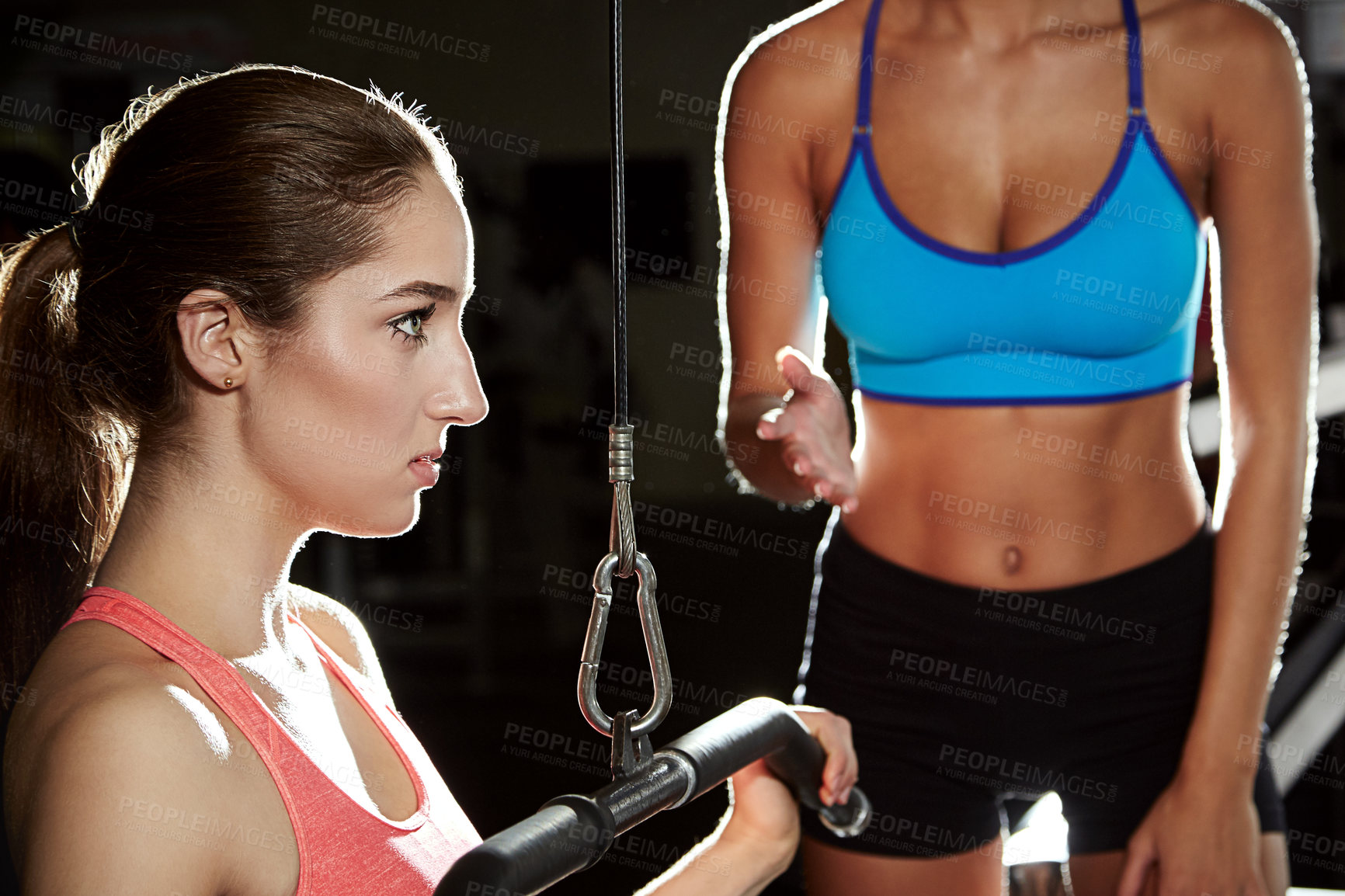 Buy stock photo Shot of a young woman working out at the gym with her trainer in the background