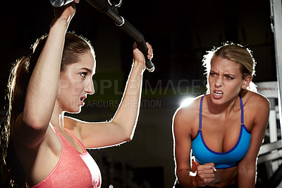 Buy stock photo Shot of a young woman working out at the gym with her friend encouraging her