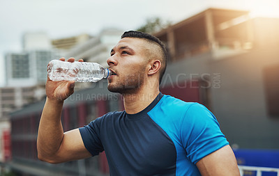 Buy stock photo Shot of a young man drinking from his water bottle while out for a run