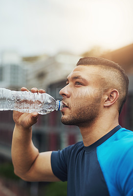 Buy stock photo Shot of a young man drinking from his water bottle while out for a run
