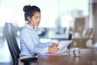 Buy stock photo Shot of a young businesswoman going over paperwork at her desk