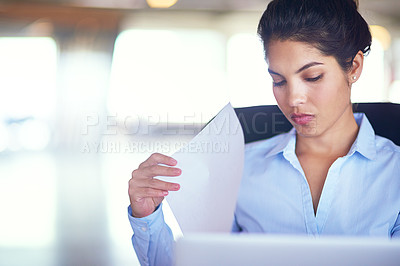 Buy stock photo Shot of a young businesswoman going over documents while working on her laptop
