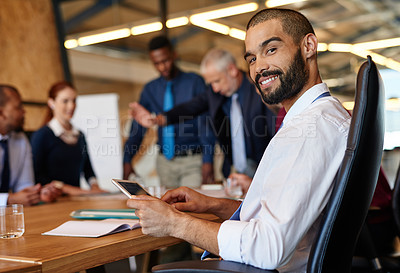 Buy stock photo Shot of a young businessman sitting with a tablet with his  colleagues working in the background