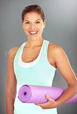 Buy stock photo Portrait of a young woman holding a yoga mat while standing against a gray background