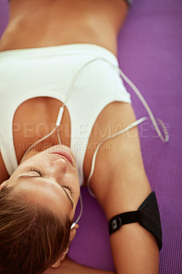 Buy stock photo Cropped shot of a sporty young woman listening to music while lying on an exercise mat