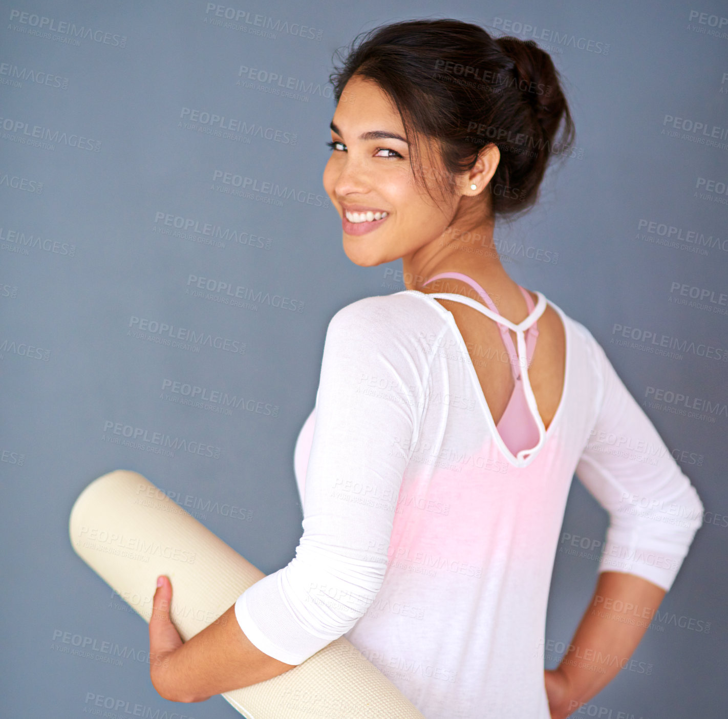 Buy stock photo Rearview shot of a sporty young woman holding her yoga mat against a grey background