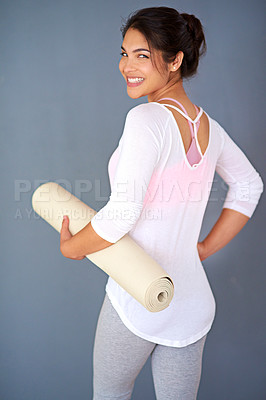 Buy stock photo Rearview shot of a sporty young woman holding her yoga mat against a grey background
