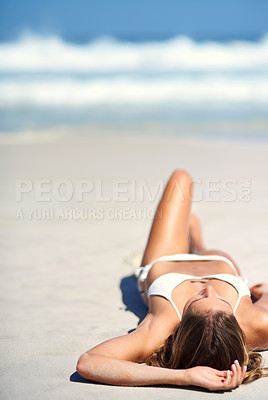 Buy stock photo Shot of an attractive young woman lying on the beach in a bikini