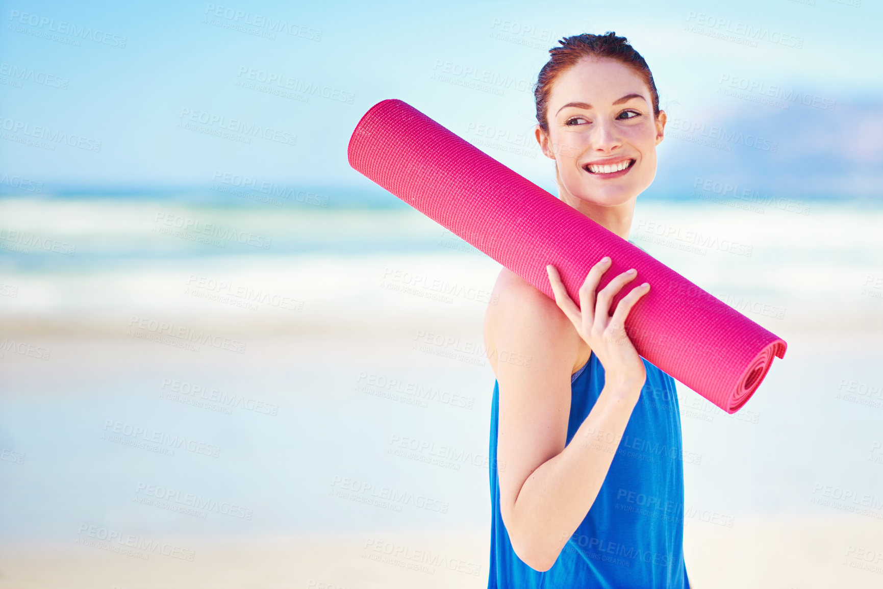 Buy stock photo Shot of a young woman holding a yoga mat while standing on the beach