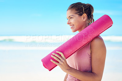 Buy stock photo Shot of a young woman holding a yoga mat while standing on the beach