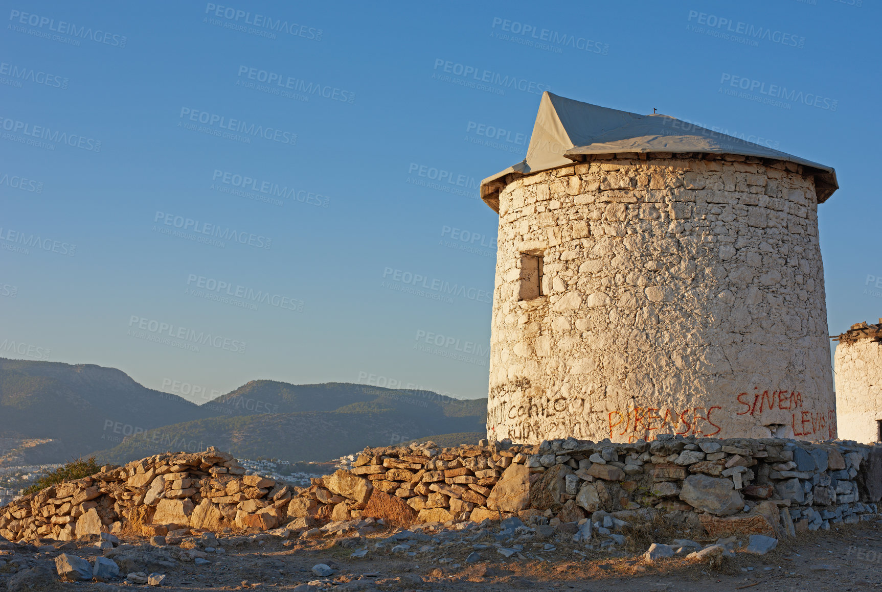 Buy stock photo Old windmill in ruin near small village or countryside. A round abandoned stone white building with green shrubby hills in the background. The architecture of an ancient sustainable wind turbine house