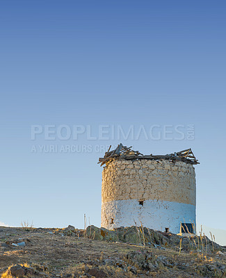 Buy stock photo Old windmill in ruin on a hill with a scenic background of the blue sky. Ancient and historic design of a watermill display of vintage architecture. The exterior of an aged stone mill with copyspace