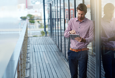 Buy stock photo Shot of a young businessman using a digital tablet outside of an office building