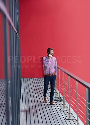 Buy stock photo Shot of a young businessman talking on a phone on the balcony of an office