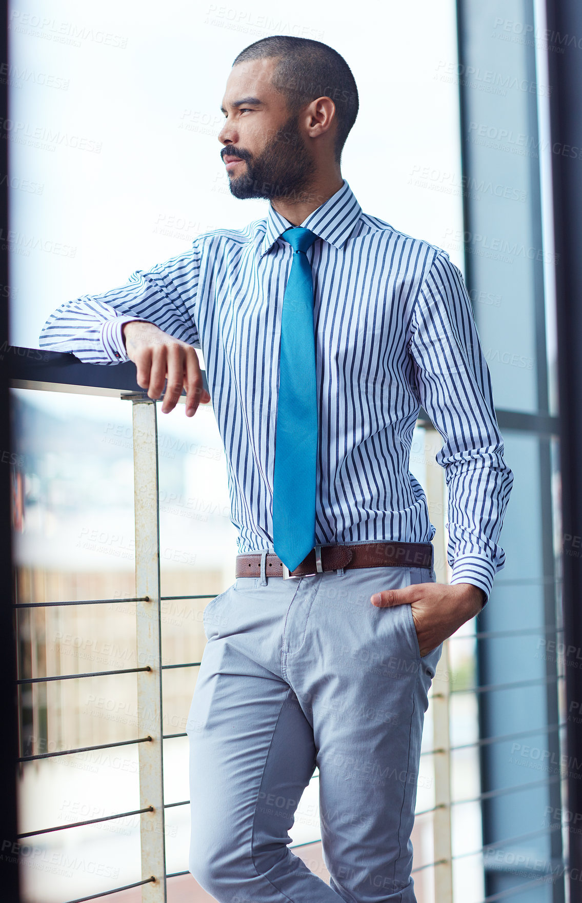 Buy stock photo Shot of a thoughtful young businessman standing on the balcony of an office building