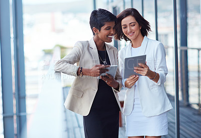 Buy stock photo Shot of two young businesswomen using a digital tablet together outside of an office building