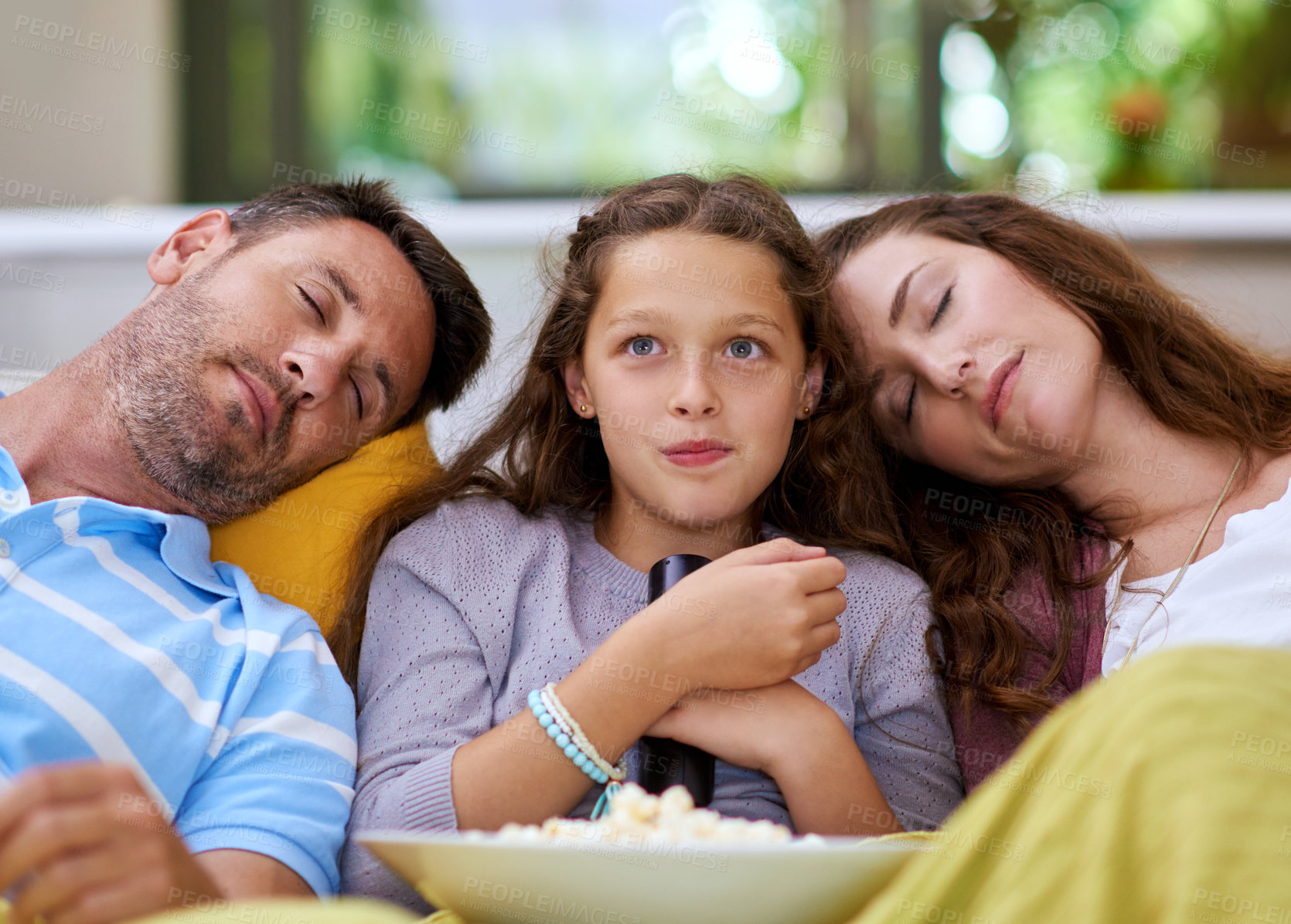 Buy stock photo Cropped shot of a young girl watching a movie while both her parents sleep on either side of her